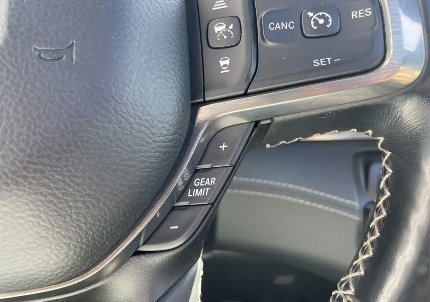 Gros plan sur la partie droite du volant noir en cuir du Dodge RAM 1500 blanc nacré, avec commandes de régulateur et limiteur de vitesse.