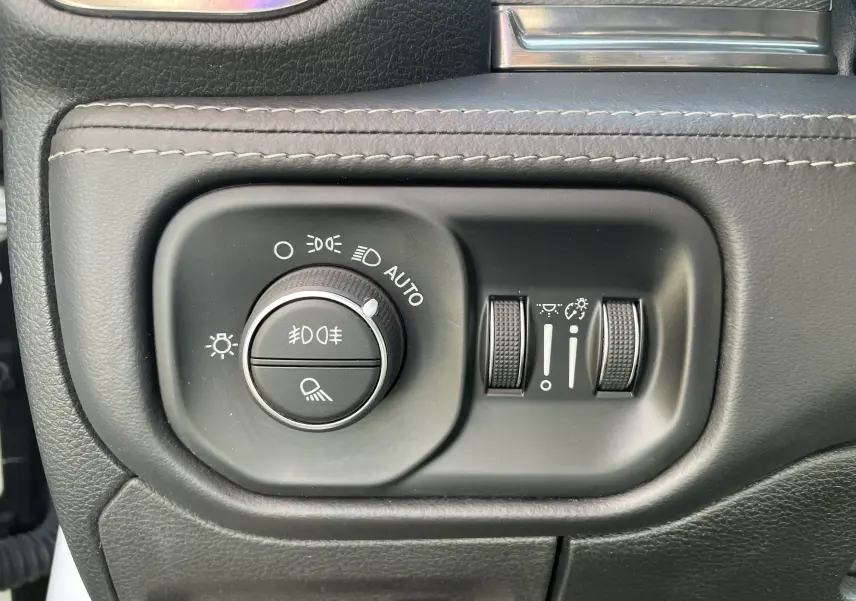 Gros plan sur les commandes d'éclairage et réglages lumineux du tableau de bord du Dodge RAM 1500 blanc nacré.
