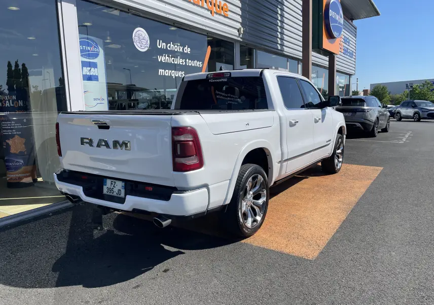 Vue 3/4 arrière droite du Dodge RAM 1500 blanc nacré avec jantes chromées et marchepied électrique visible.