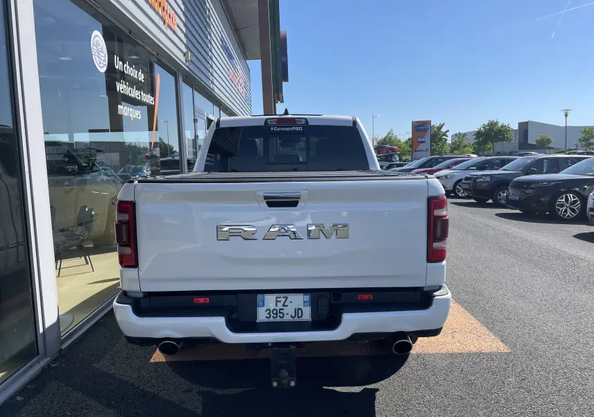 Vue arrière d'un pick-up Dodge RAM 1500 blanc nacré avec logo chromé et double sortie d'échappement visible.