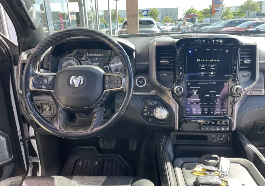 Vue intérieure du tableau de bord et volant du Dodge RAM 1500 blanc nacré avec écran tactile central et commandes au volant.