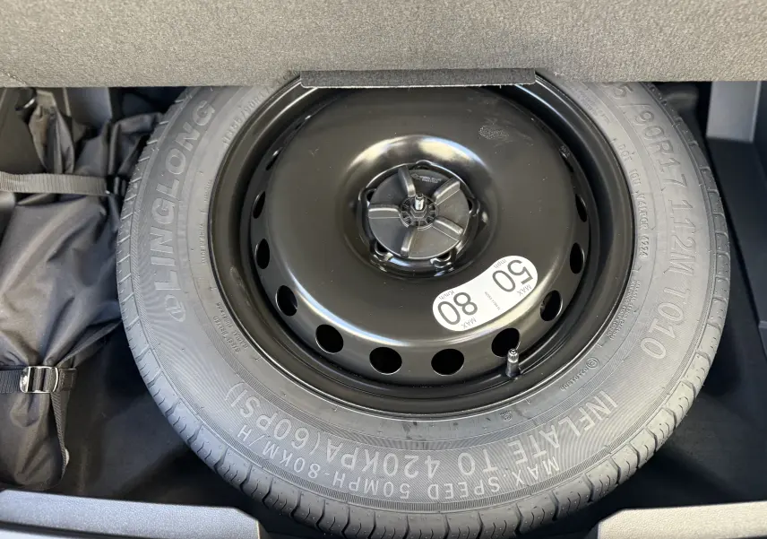 Pneu de secours noir avec étiquette de limitation de vitesse, logé dans le coffre d'une Renault Austral blanc nacré toit noir.