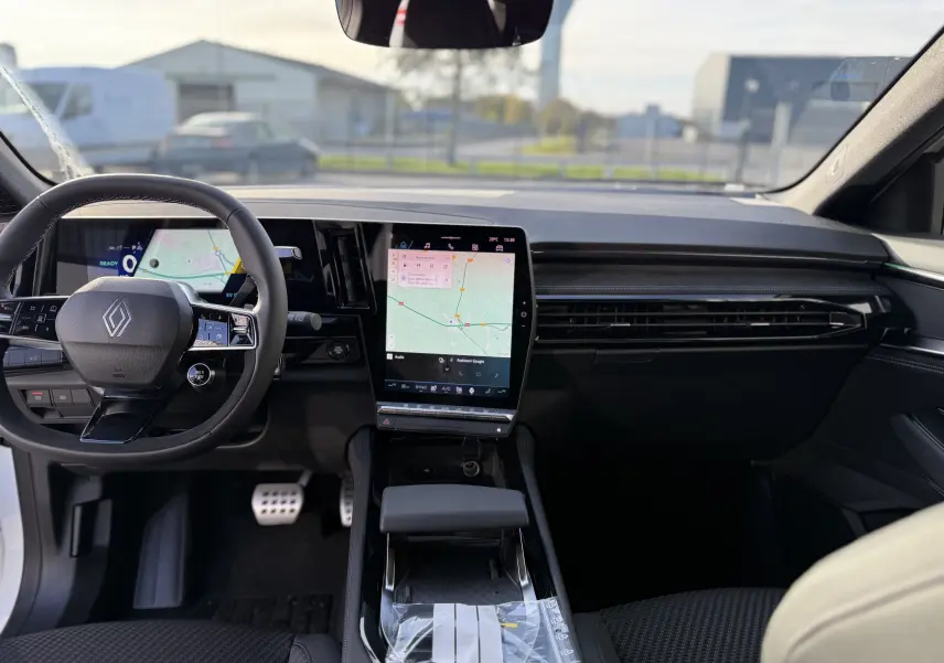 Vue intérieure avant du Renault Austral blanc nacré, mettant en valeur le tableau de bord moderne avec écran tactile central vertical.