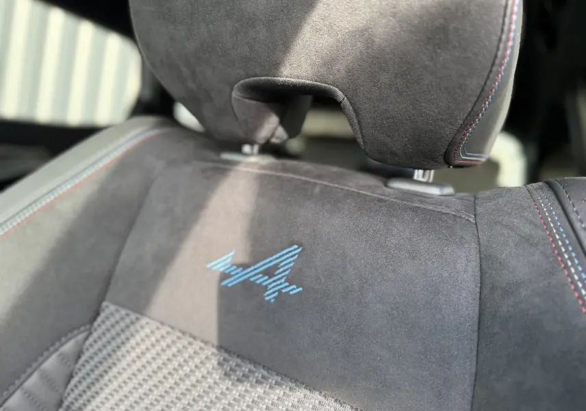 Gros plan sur le siège avant en alcantara noir avec logo Alpine bleu et surpiqûres tricolores du Renault Austral 2025.