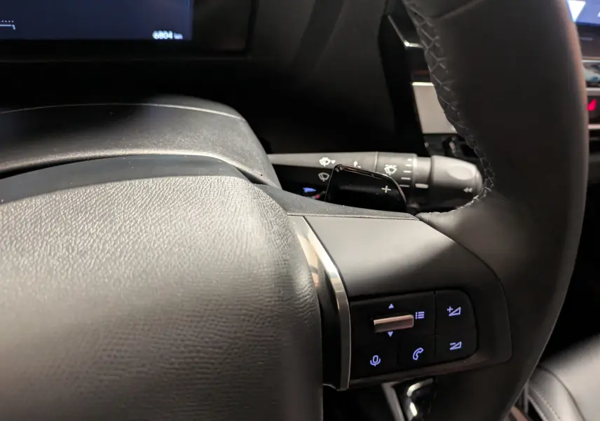 Gros plan sur le volant noir du Citroën C4 Hybride 2025, avec commandes intégrées et palettes au volant visibles.