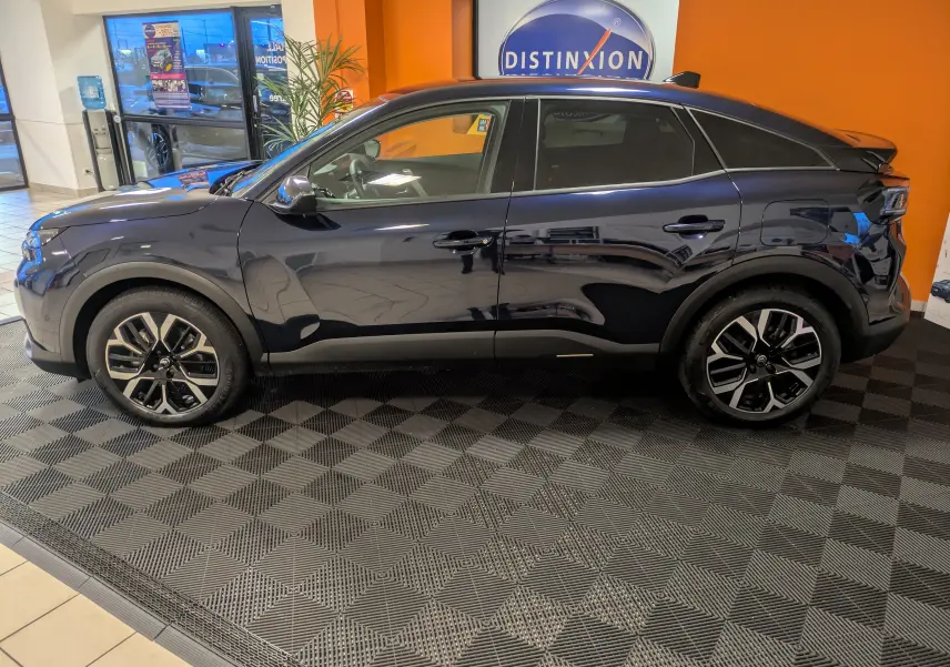 Vue latérale gauche d'une Citroën C4 hybride bleu nuit 2025 en showroom avec jantes alliage 18 pouces bicolores.