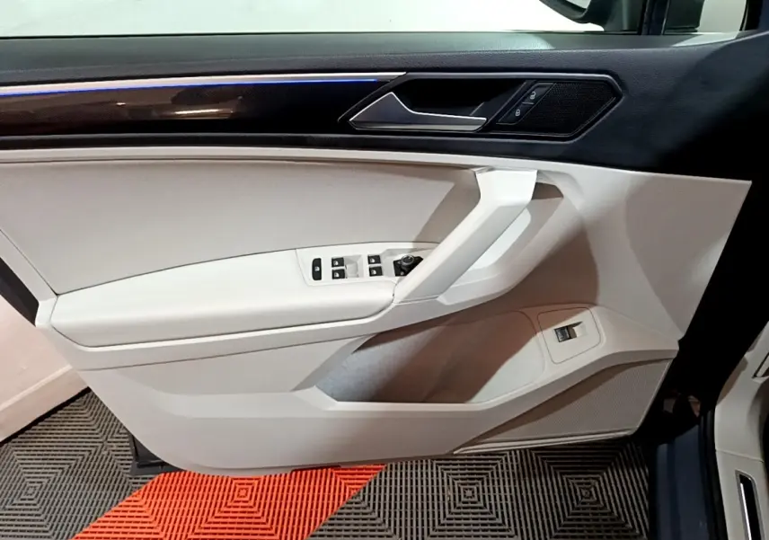 Vue intérieure côté gauche de la porte avant gris clair du Volkswagen Tiguan 2.0 TDI 150 DSG7 Elegance avec éclairage d’ambiance bleu.