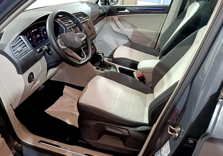 Vue intérieure côté conducteur du Volkswagen Tiguan gris clair 2022, avec sièges bicolores et tableau de bord digital.