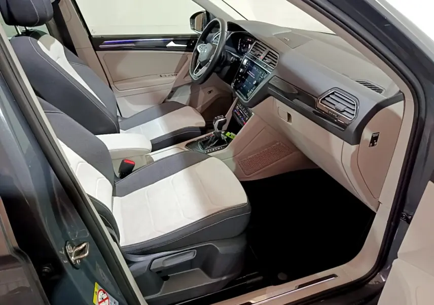Vue intérieure côté conducteur du Volkswagen Tiguan gris clair 2022, sièges bicolores et tableau de bord moderne avec écran tactile.