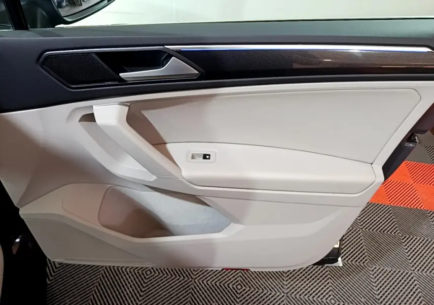 Intérieur côté gauche de la porte avant du Volkswagen Tiguan gris clair, avec poignée et panneau beige clair.