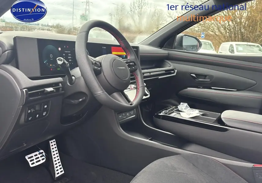 Vue intérieure côté conducteur du Hyundai Tucson 2026, volant cuir avec surpiqûres rouges et tableau de bord digital.