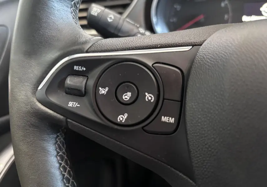 Gros plan sur les commandes de régulateur de vitesse au volant noir de l’Opel Grandland rouge foncé.