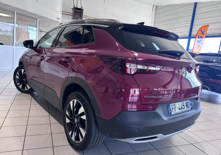 Vue 3/4 arrière droite d’un Opel Grandland X rouge foncé avec jantes alliage noires et toit noir en showroom.