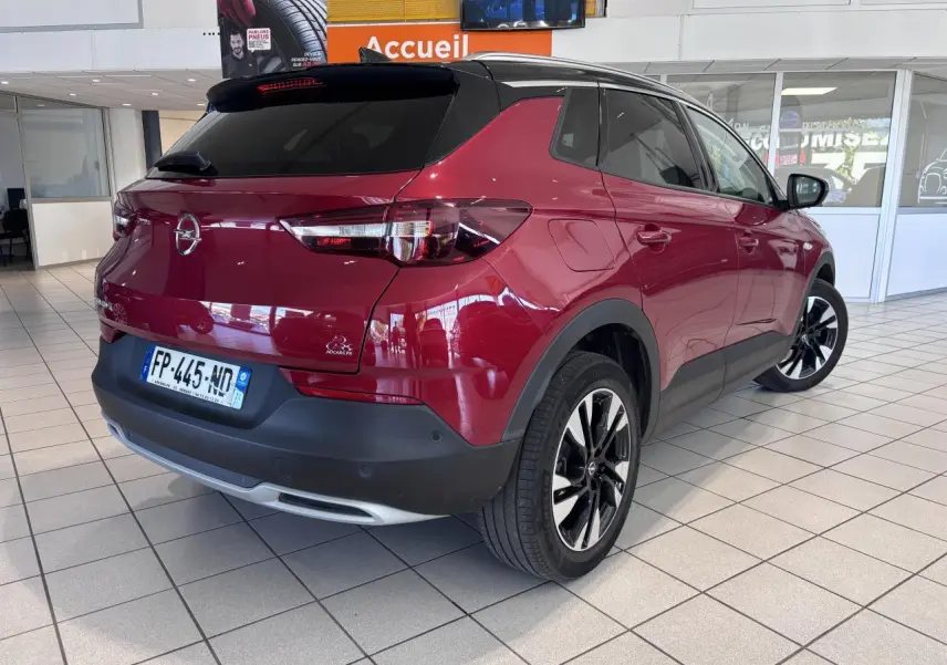 Vue 3/4 arrière droite d'un Opel Grandland rouge foncé avec toit noir et jantes alliage 19 pouces en showroom.