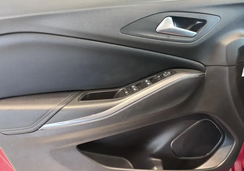 Vue rapprochée de la porte avant gauche noire avec commandes électriques et haut-parleur d’un Opel Grandland rouge foncé.