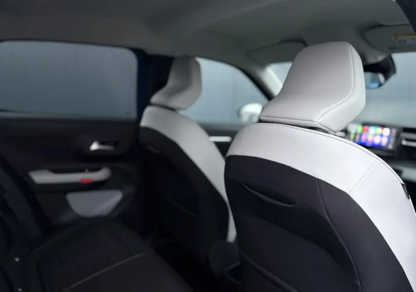 Vue intérieure arrière droite de la Citroën C3 2025 avec sièges bicolores noir et blanc et écran tactile central visible.