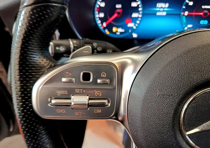 Gros plan sur le volant cuir et alu du Mercedes GLC 300 E AMG Line 2021 avec commandes intégrées et tableau de bord numérique bleu.