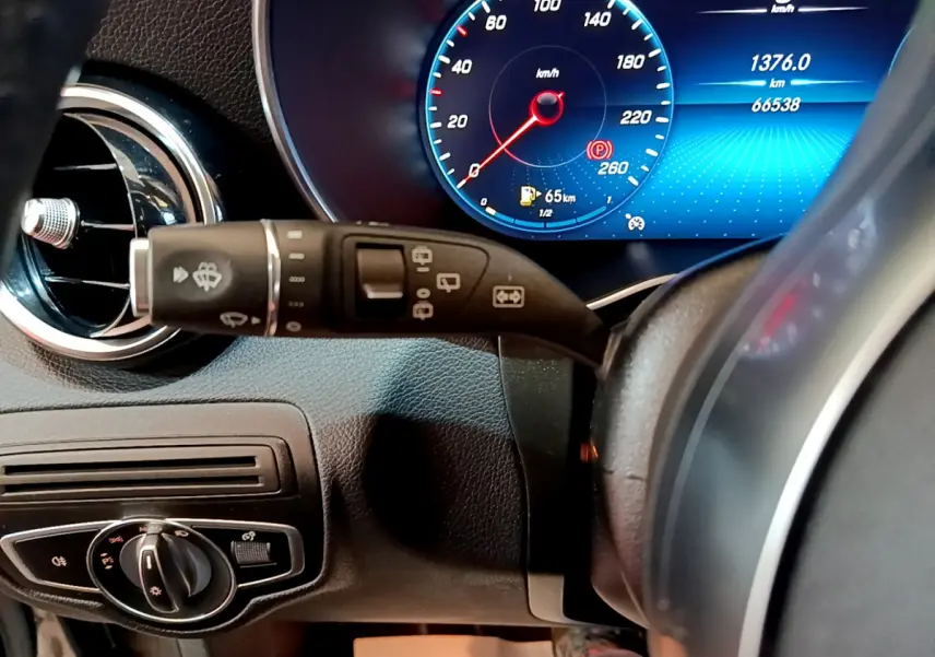 Gros plan sur le combiné d'instruments numérique bleu et le commodo de phares dans l'habitacle gris foncé d'une Mercedes GLC 300 E AMG Line 2021.