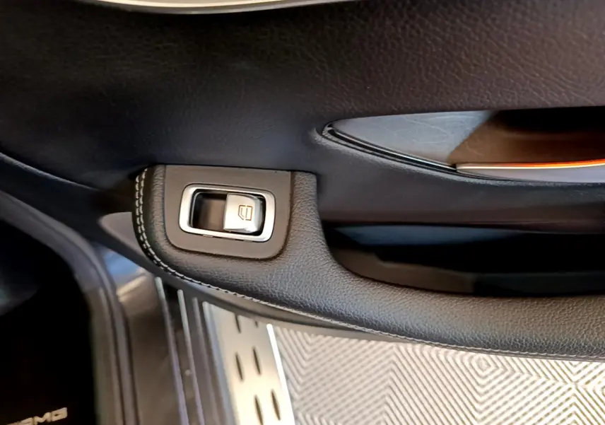 Gros plan sur la commande de lève-vitre en cuir noir avec surpiqûres dans une Mercedes GLC 300 E AMG Line gris foncé.