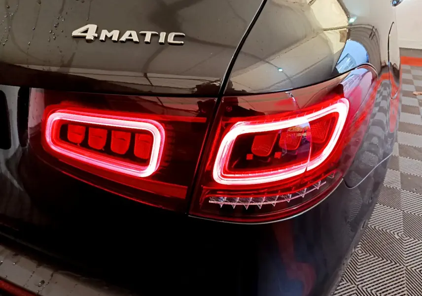 Gros plan sur le feu arrière droit rouge allumé et le logo 4MATIC sur la carrosserie gris foncé d'un Mercedes GLC hybride.