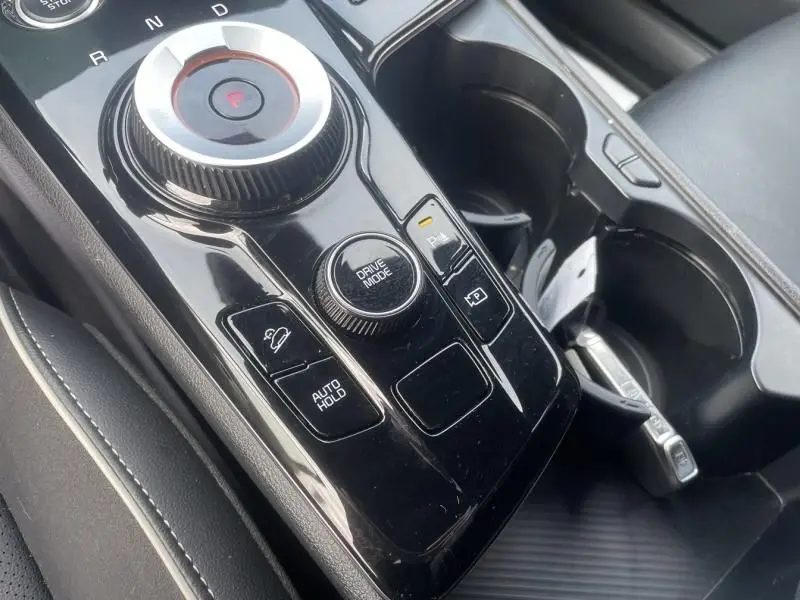Gros plan sur la console centrale noire brillante du Kia Sportage 2022, montrant la molette de sélection de vitesse et les boutons de contrôle.