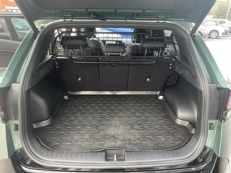 Coffre ouvert vu de l'arrière d'un KIA Sportage vert métal 2022 avec grille de séparation et tapis de coffre.