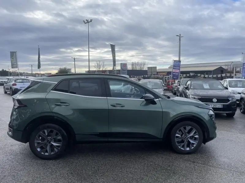 Vue de profil côté gauche d'un KIA SPORTAGE 1.6 T-GDI 230 CV GT-LINE PREMIUM vert métal avec jantes alliage, en extérieur sur parking.