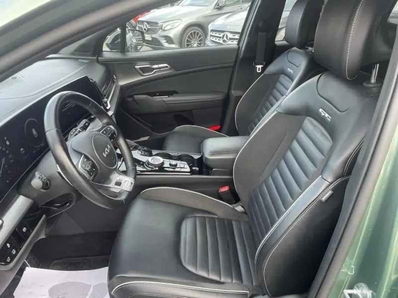 Vue intérieure côté conducteur du KIA SPORTAGE 1.6 T-GDI 230 CV GT-LINE PREMIUM 2022, sièges cuir noirs avec logo GT-LINE, portière vert métal visible.