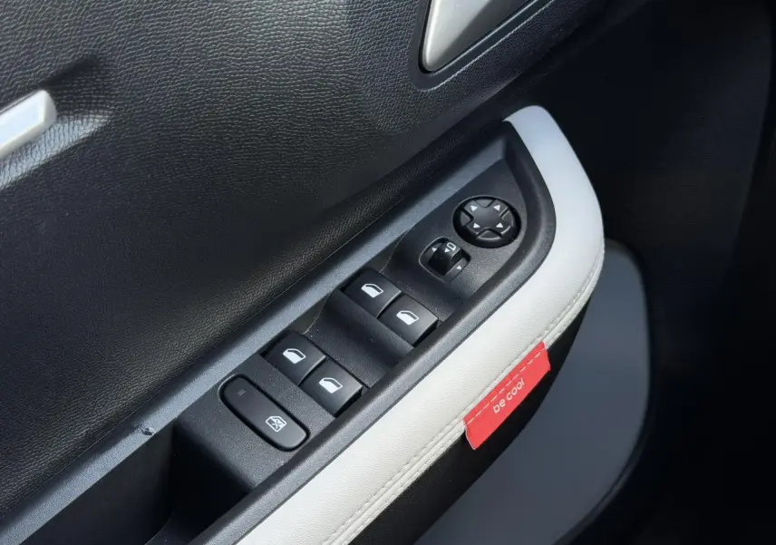 Gros plan sur la commande des vitres électriques côté conducteur avec surpiqûres blanches et étiquette rouge "be cool" sur la portière.