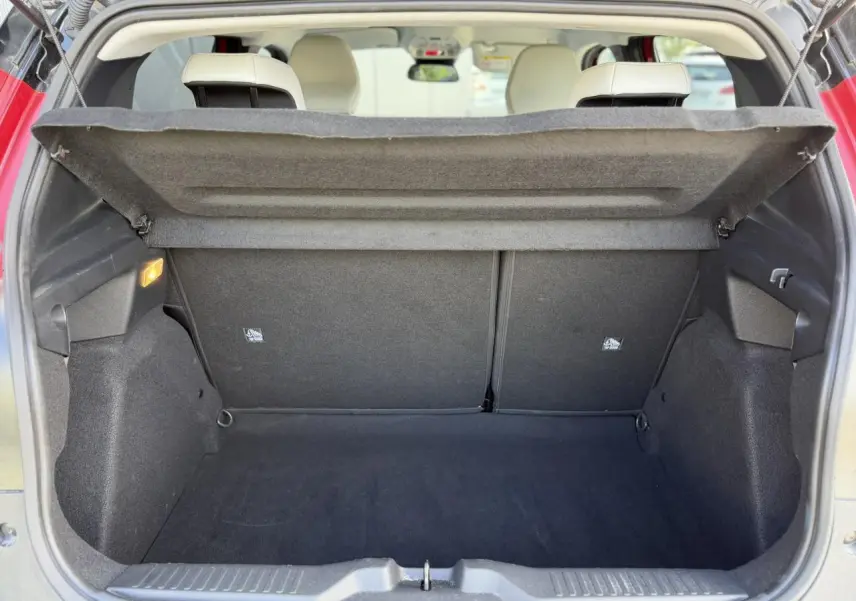 Vue intérieure du coffre ouvert d'une Citroën C3 Rouge Elixir, montrant l'espace de rangement et les sièges arrière beiges.
