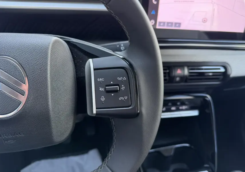 Gros plan sur la commande gauche du volant noir de la Citroën C3 2025, avec écran GPS visible en arrière-plan.