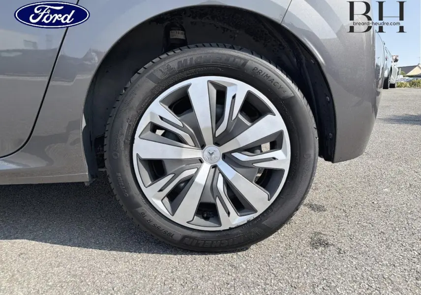 Gros plan sur la roue avant gauche d'une Peugeot 208 gris Platinium avec enjoliveur et logo lion central.