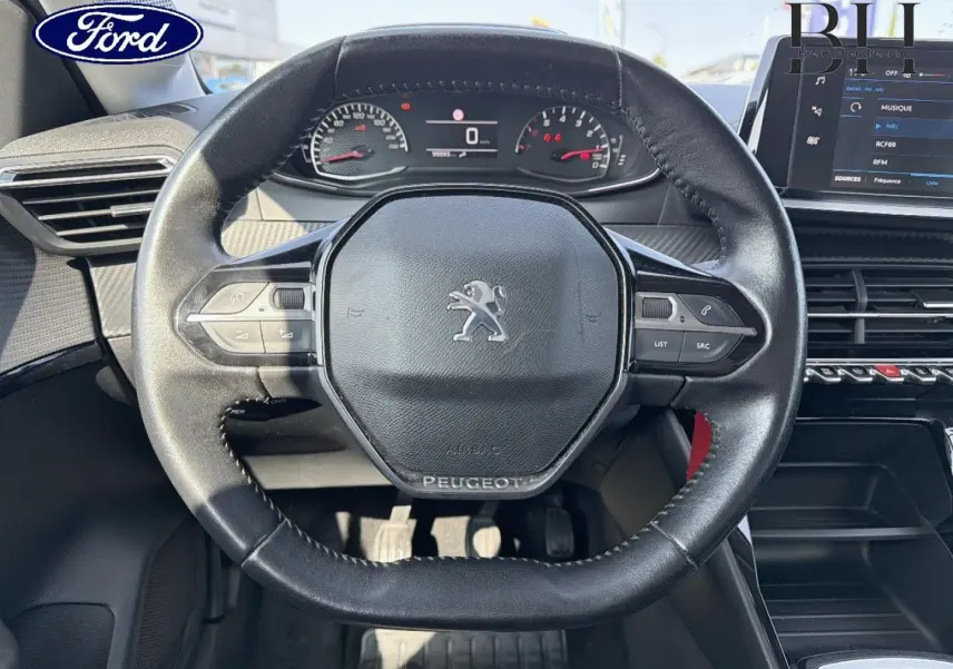 Vue rapprochée du volant noir de la Peugeot 208 1.5 BlueHDi avec tableau de bord et écran tactile visibles.