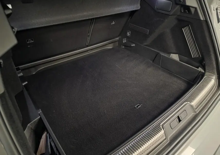 Coffre ouvert du DS7 Crossback gris, montrant le tapis de sol et les rangements latéraux noirs.