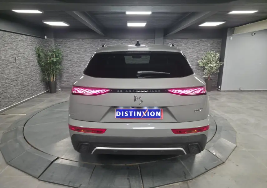 Vue arrière du DS7 Crossback gris métallisé avec feux arrière LED 3D et logo DS Automobiles sur fond intérieur showroom.