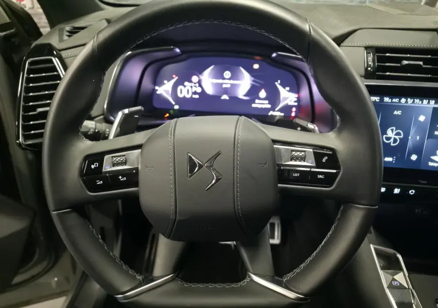 Vue rapprochée du volant en cuir noir du DS7 Crossback 2025 avec commandes intégrées et tableau de bord numérique lumineux.