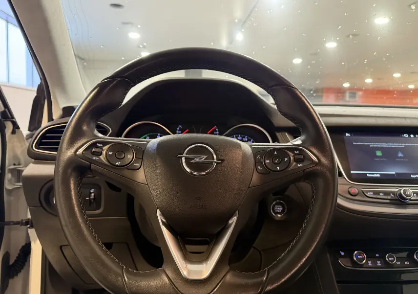 Vue centrée sur le volant en cuir noir d’un Opel Grandland X hybride blanc, avec tableau de bord et écran tactile visibles.