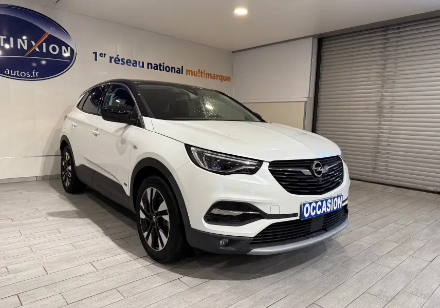 Opel Grandland X blanc vue 3/4 avant droit en intérieur, avec toit noir et jantes alliage bicolores.