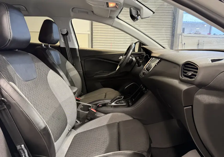 Vue intérieure côté gauche de l’Opel Grandland X 1.6 Hybrid Turbo 2021, sièges tissu noir et gris avec console centrale visible.