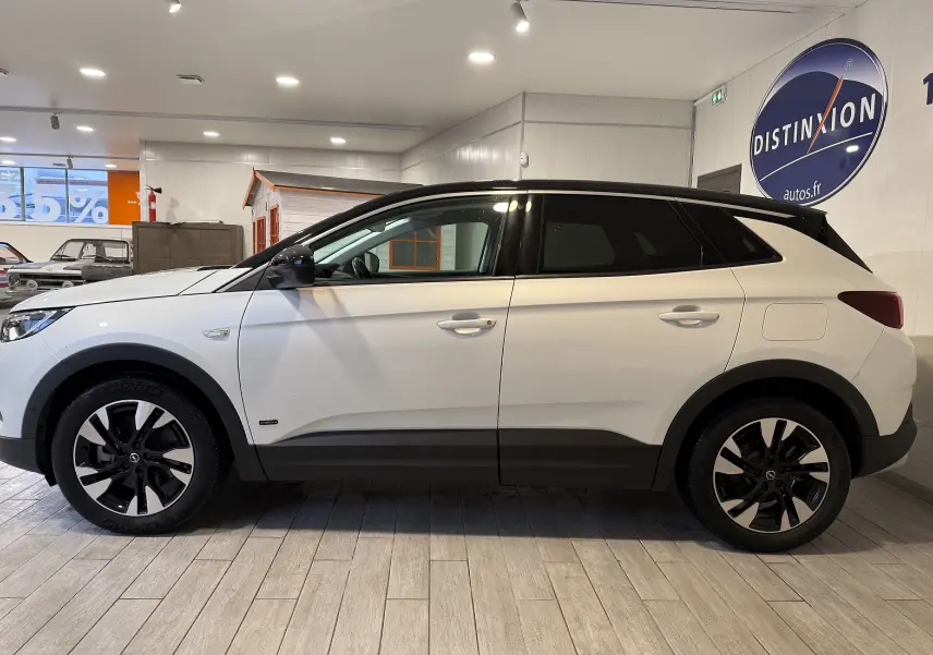 Vue de profil côté gauche d'un Opel Grandland X blanc hybride rechargeable avec jantes noires et toit noir en intérieur showroom.