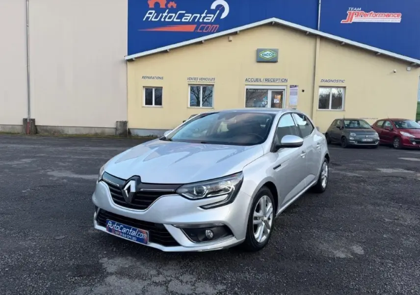Renault Mégane gris alu vue 3/4 avant droit, avec phares LED et jantes alliage, stationnée devant un garage AutoCantal.