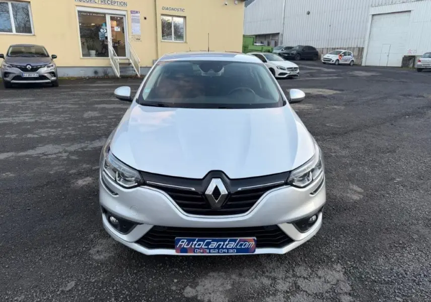 Vue avant d'une Renault Mégane gris alu 2019, avec calandre noire et phares LED visibles, stationnée devant un bâtiment.