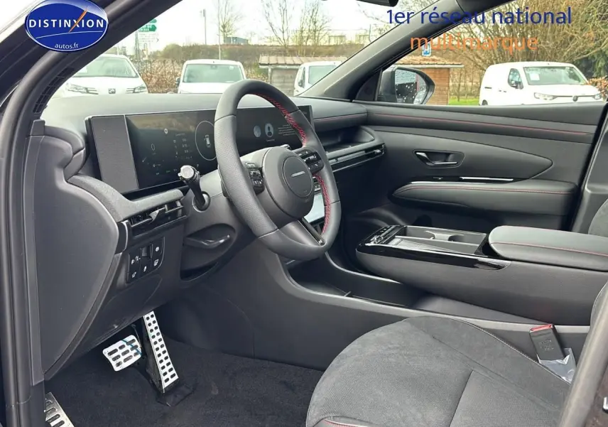 Vue intérieure côté conducteur du Hyundai Tucson 2026 noir, volant cuir avec surpiqûres rouges et tableau de bord numérique.