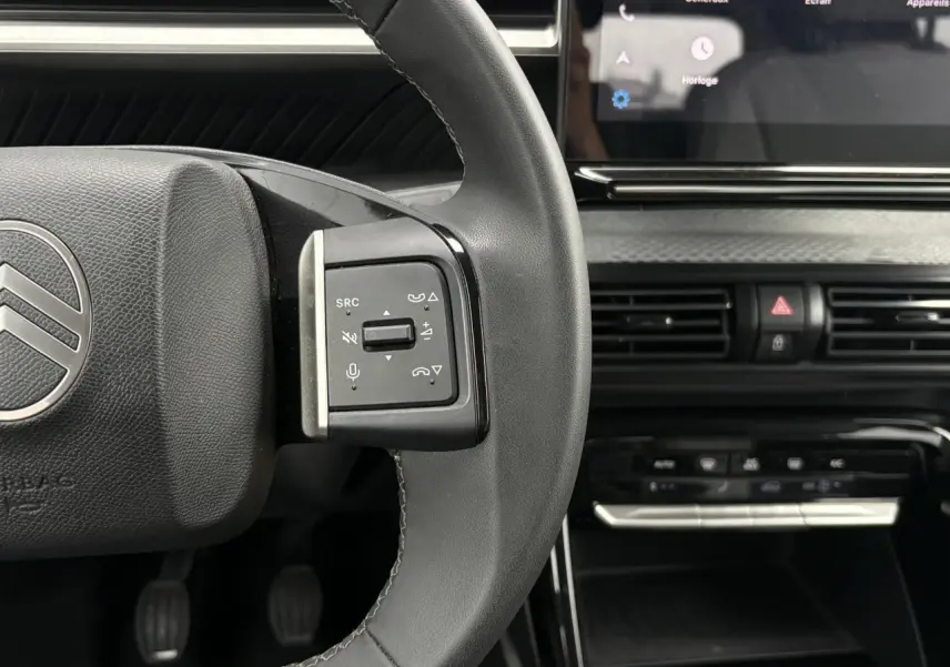 Gros plan sur le volant noir de la Citroën C3 2025 avec commandes audio et écran tactile en arrière-plan.