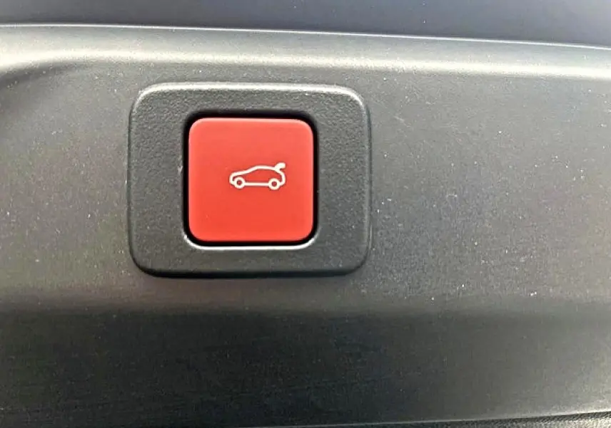Bouton rouge d'ouverture électrique du coffre sur un Peugeot 3008 gris titane, vue en gros plan intérieur.