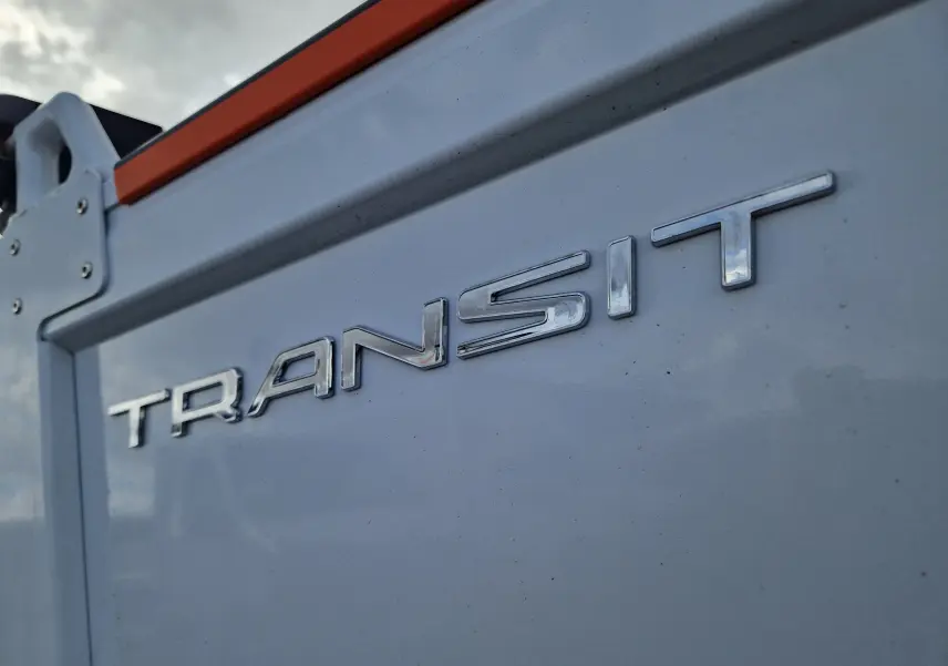 Gros plan sur l’inscription chromée "TRANSIT" sur la benne blanche du Ford Transit Chassis Cabine, angle latéral rapproché.