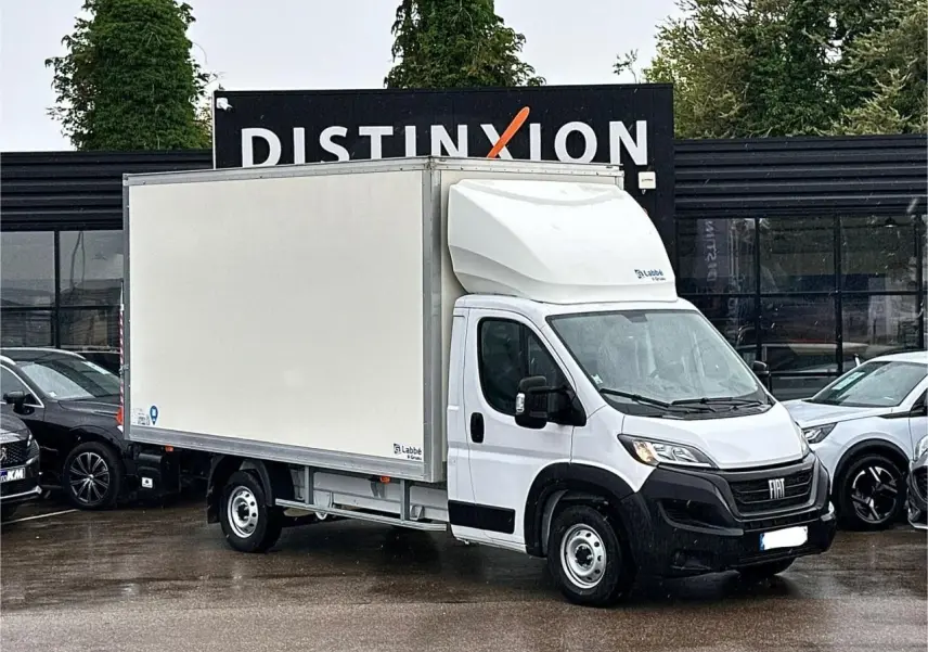 Fiat Ducato Fourgon blanc vu de trois quarts avant droit avec caisse capucine sur parking humide.