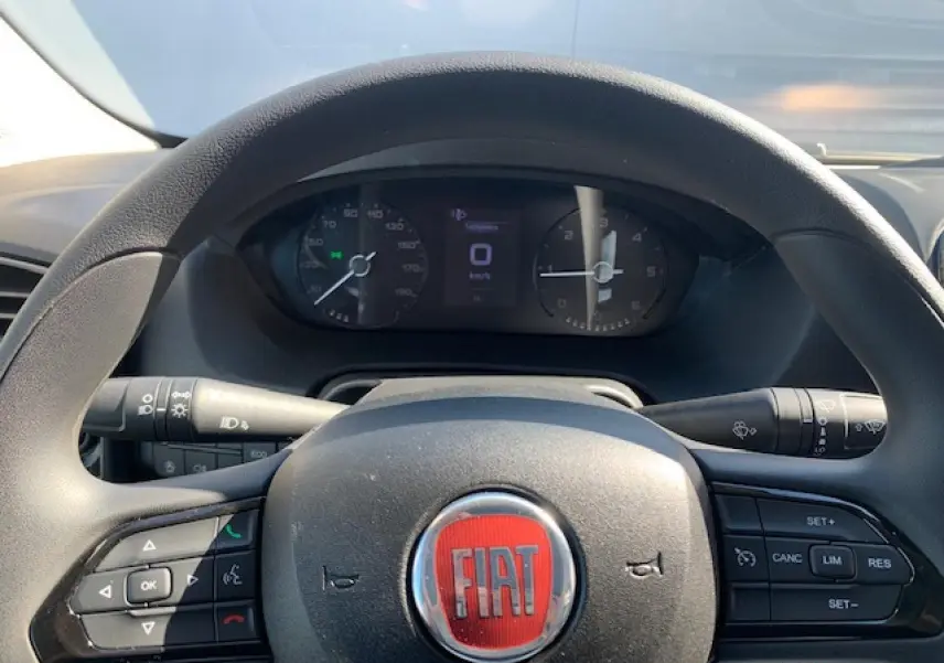 Vue rapprochée du volant noir avec logo rouge FIAT et tableau de bord digital du Fiat Ducato Fourgon blanc 2022.