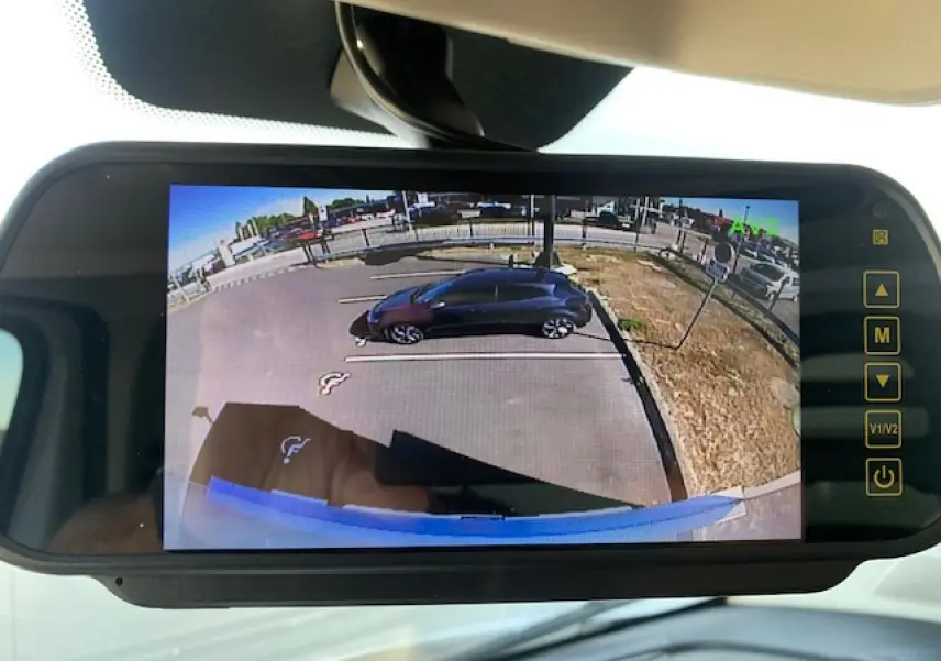 Écran de rétroviseur numérique montrant une vue arrière du parking avec un véhicule noir stationné à droite.