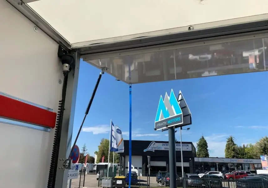 Vue partielle intérieure du hayon ouvert d'un fourgon blanc FIAT Ducato Business, avec ciel bleu et enseigne Attractiv Motors en arrière-plan.